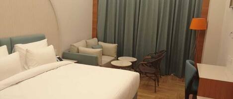 A hotel room with a large bed, a small sofa, two chairs, a round table, and a curtain.