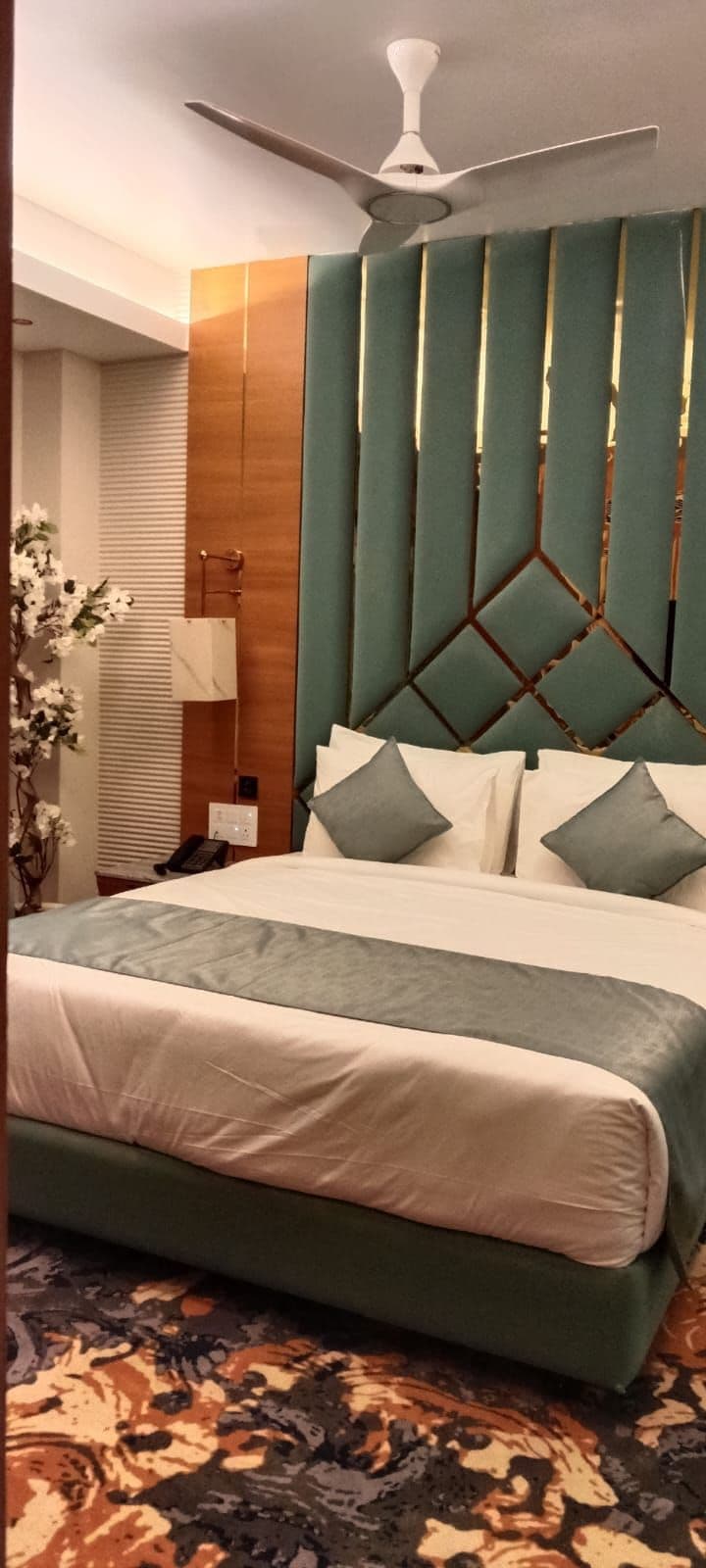 Une chambre d’hôtel avec un lit, un ventilateur de plafond, une table de chevet et une lampe fixée au mur.
