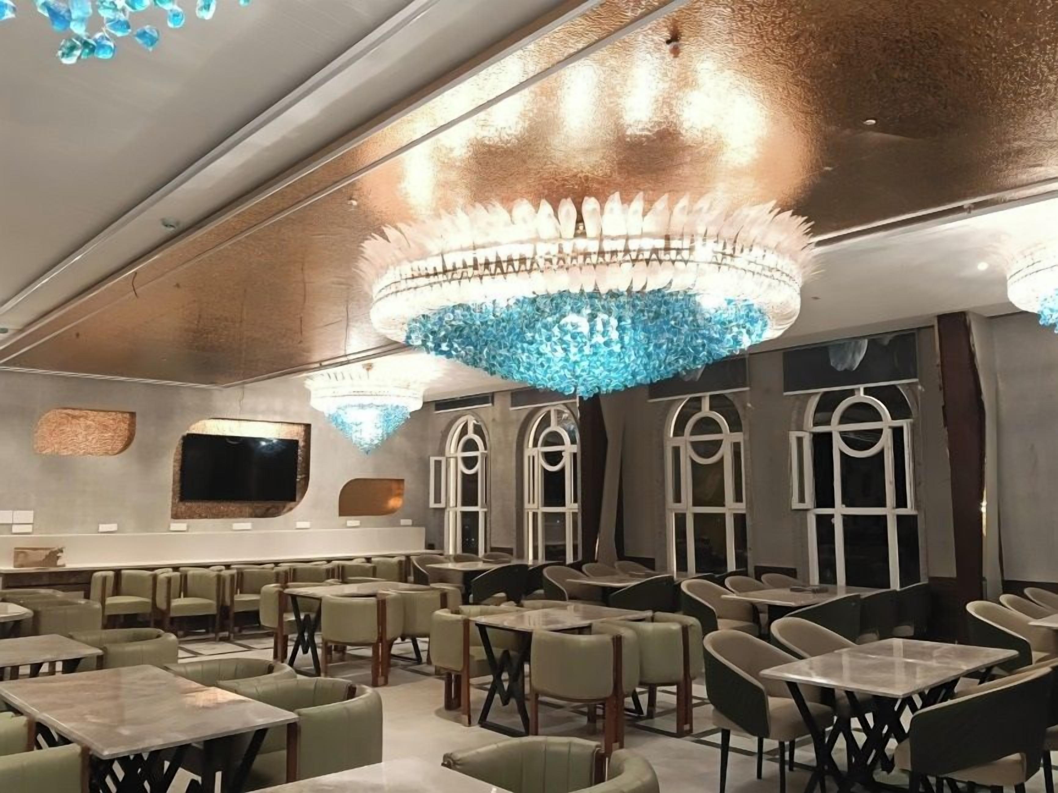Een restaurant met meerdere tafels en stoelen, een grote kroonluchter en boogvensters.