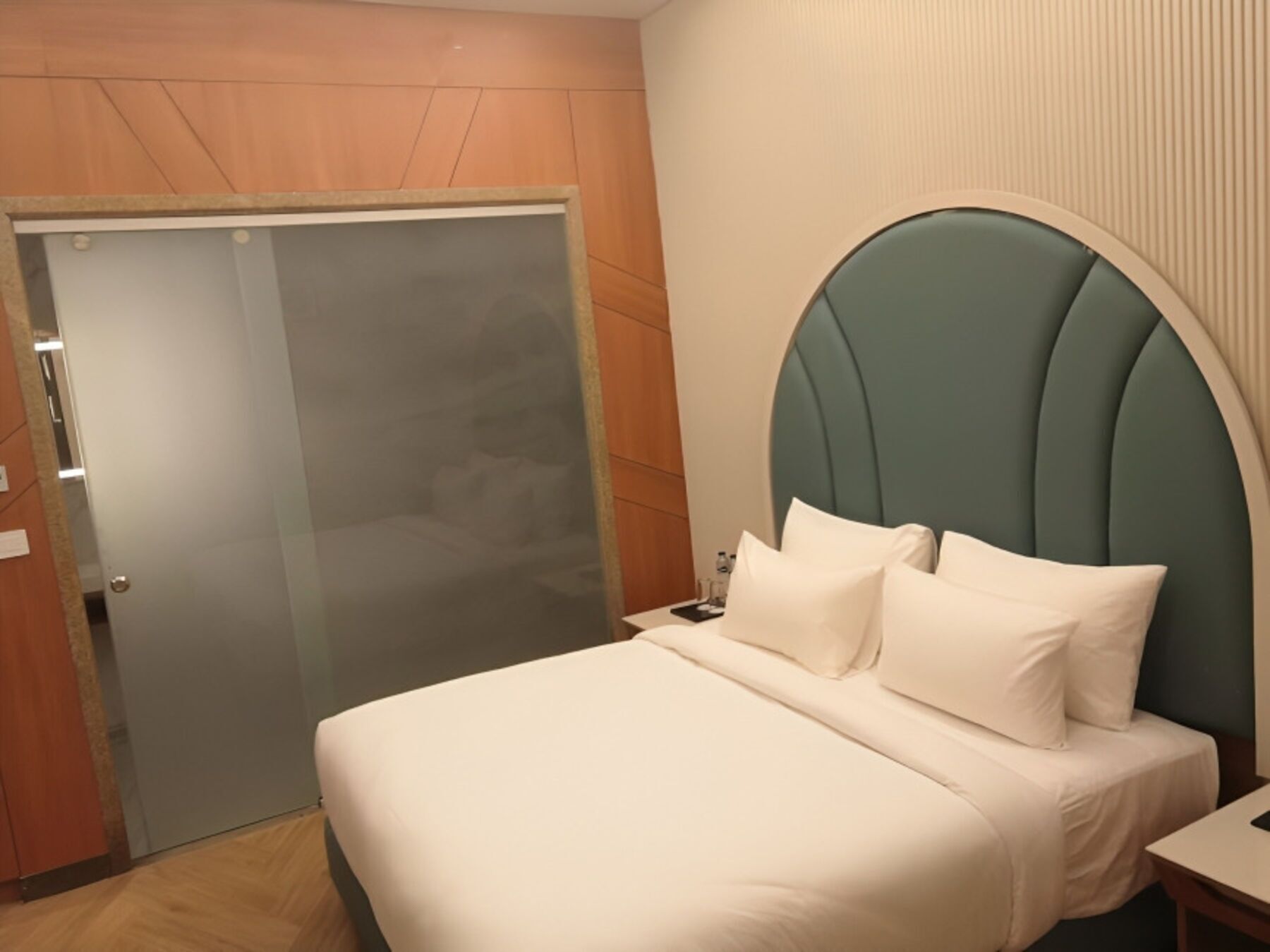 A hotel room with a bed, a nightstand, a door, and a wall with a textured pattern.
