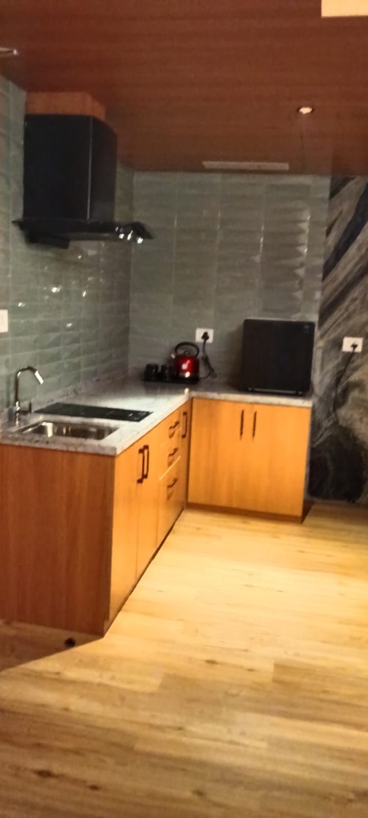 Une cuisine avec des meubles de rangement en bois, un évier et une bouilloire rouge.