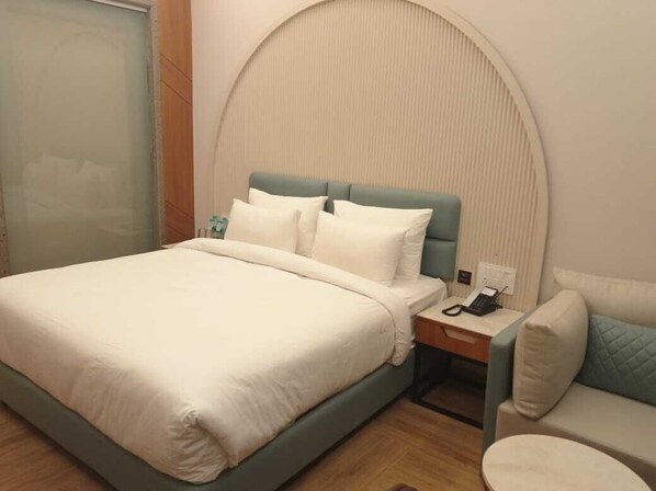 Una cama bien hecha con sábanas blancas, una mesita de noche con un teléfono y una silla con cojín.