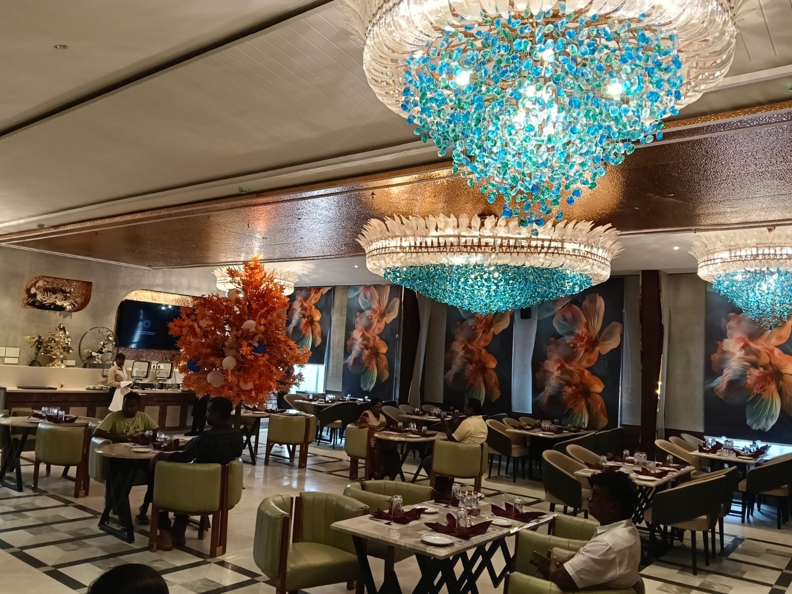 A restaurant interior with multiple dining tables, chairs, and a large decorative chandelier.