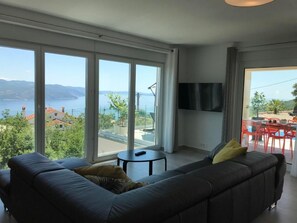 Ein modernes Wohnzimmer mit großem Fenster, einer Couch, einem kleinen Tisch und einem Flachbildfernseher.