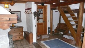 Een rustiek interieur met een houten trap, een bankje, een dressoir en een betegelde vloer.