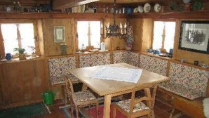 Een houten eetkamer met een tafel en banken, een betegelde vloer en een vloerkleed met dessin.