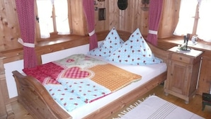 Een slaapkamer in een houten hut met een bed, kussens, een klein tafeltje en een raam.