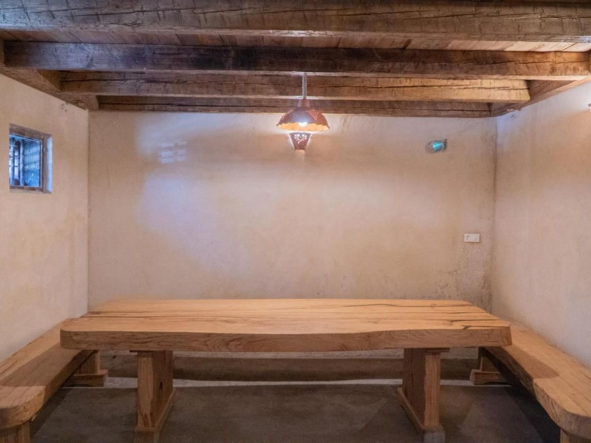 Una stanza con un tavolo di legno, panche, una piccola finestra e un portalampada a parete.