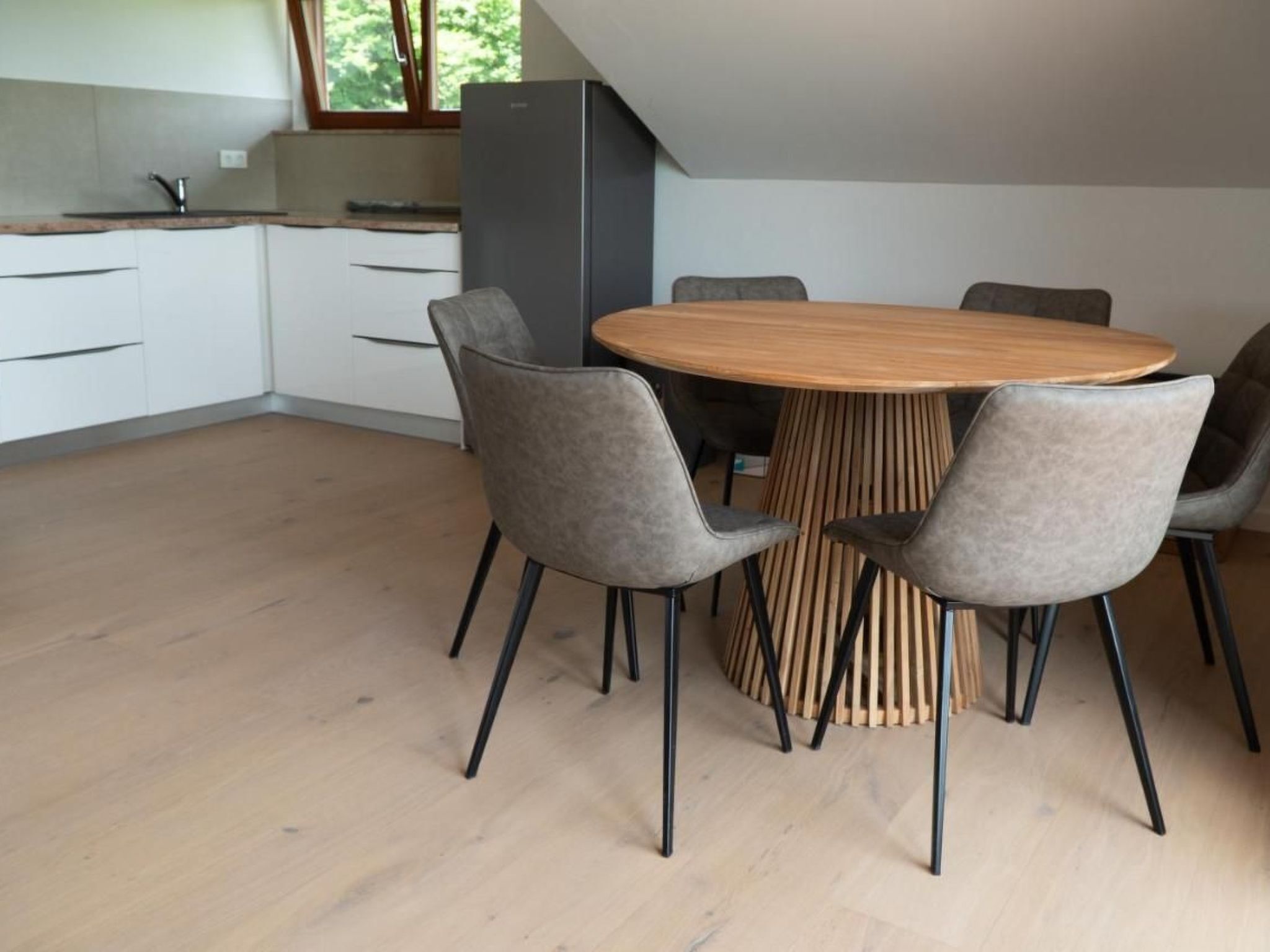 A modern kitchen with white cabinets, a wooden dining table, and six grey chairs.