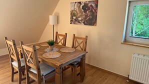 Zona pranzo con tavolo in legno, sei sedie, una lampada da terra e un quadro appeso al muro.
