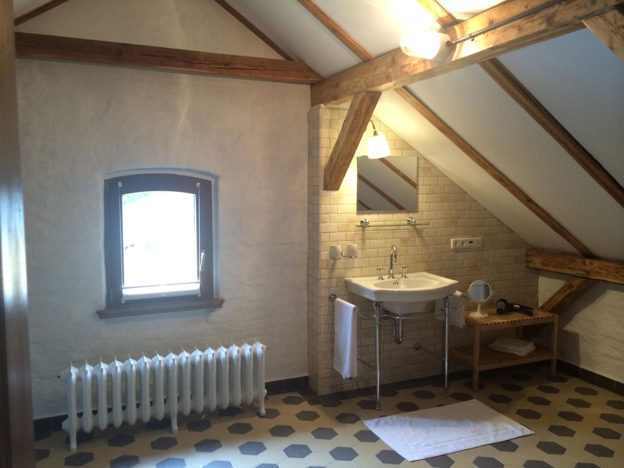 A small, well-lit attic bathroom with a window, a radiator, a sink, and a mirror.