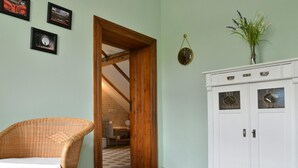 Una habitación con una silla de mimbre, un aparador blanco con paneles de cristal decorativos y una puerta de madera que da a otra habitación.