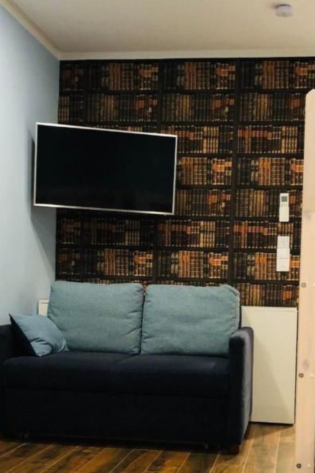 Una sala de estar con un sofá negro, dos cojines azul claro y un televisor de pantalla plana montado en una pared estampada.