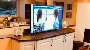 A kitchen with a large flat-screen TV, white cabinets, and a wooden countertop. - Schwimmendes Haus Elandi by Interhome (Bitterfeld)