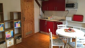 Eine kleine Küche mit Holzbalken, roten Schränken, einer Mikrowelle und einem weißen Tisch mit Stühlen.