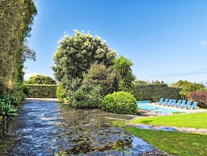Um jardim com piscina, espreguiçadeiras e um pequeno riacho.