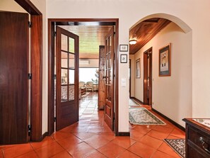 Um corredor com portas de madeira, chão de azulejos e teto com vigas de madeira.