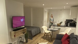 Moderni olohuone, jossa on sohva, televisio, ruokailutila pöytineen ja tuoleineen sekä keittiö, jossa on mikroaaltouuni ja kahvinkeitin.