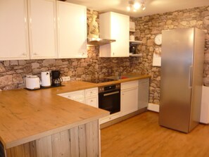 Eine Küche mit weißen Schränken, einer Steinwand, einer Holztischplatte und einem Edelstahl-Kühlschrank.