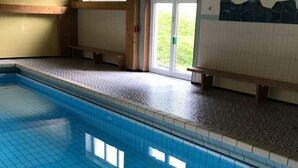 Une piscine avec un revêtement de sol en carrelage, des poutres en bois au plafond et une vue sur l’extérieur grâce à une porte vitrée.