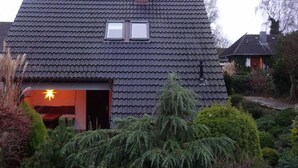 Una casa con techo de tejas oscuras, una chimenea y un ventanal pequeño.