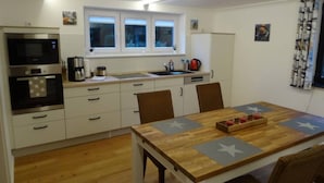 Cocina compacta con zona de comedor, que incluye una mesa de madera, sillas, horno empotrado y una ventana sobre el fregadero.