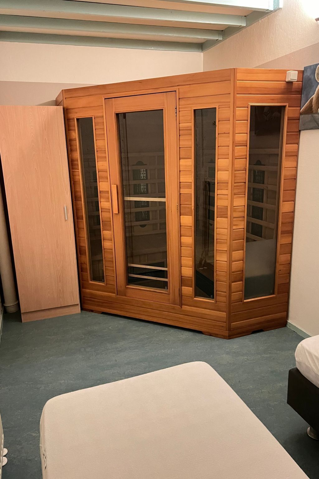 A room with a wooden wardrobe, a bed, and a small table.