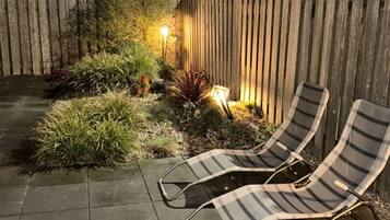 A patio with two lounge chairs, a wooden fence, and a garden area with plants and a lamp post.