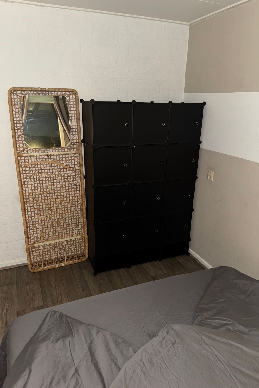 Une chambre avec un lit, un meuble de rangement noir et un panier en osier avec un miroir.