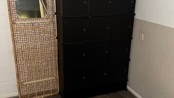 Une chambre avec un lit, un meuble de rangement noir et un panier en osier avec un miroir.