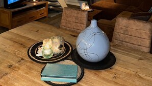 Un salon chaleureux avec une table en bois, un vase bleu et un téléviseur posé sur un meuble en bois.
