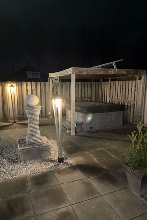 Un espace extérieur aménagé en terrasse, agrémenté d’une sculpture en pierre, d’une pergola en bois et d’un jacuzzi.