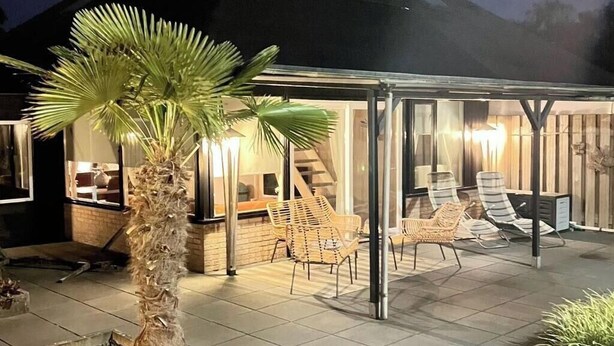 Un espace extérieur aménagé en patio, avec un coin salon couvert, un palmier et un mur de briques en arrière-plan.