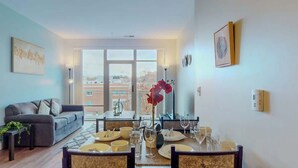A dining area with a table set for four, a sofa, and a view of the city through large windows. - Stylish Home With Free ParkingZA (Stamford)