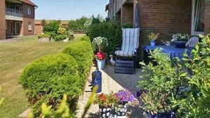 Asuinrakennuksessa on patio, jossa on pöytä ja tuolit. Patiota ympäröivät ruukuissa olevat kasvit ja pieni puutarha.