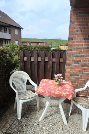Eine Terrasse mit zwei weißen Plastikstühlen und einem Tisch mit einer blumigen Tischdecke.