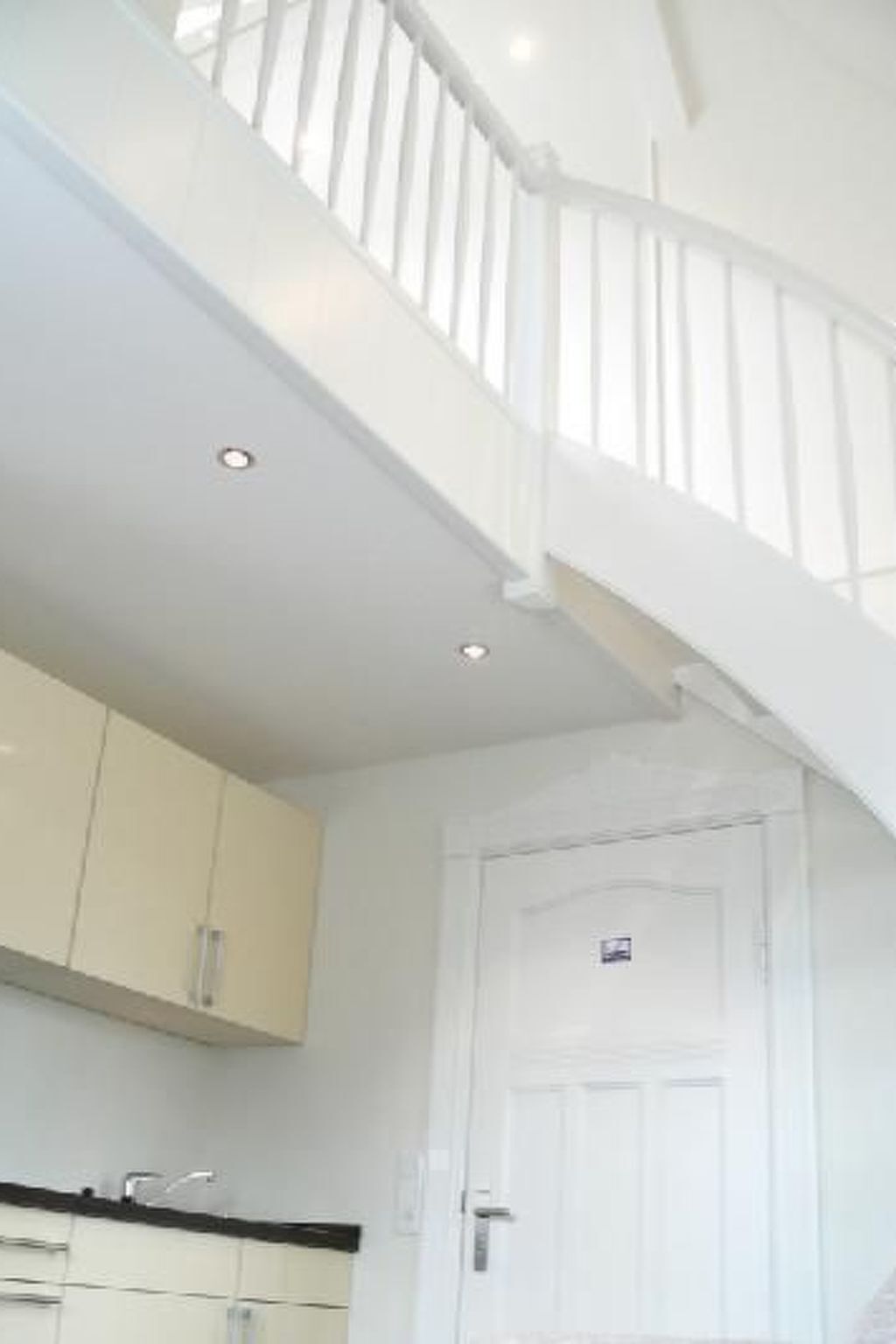 A staircase with white railings leading to a landing. There is a white door with a small window on the landing.