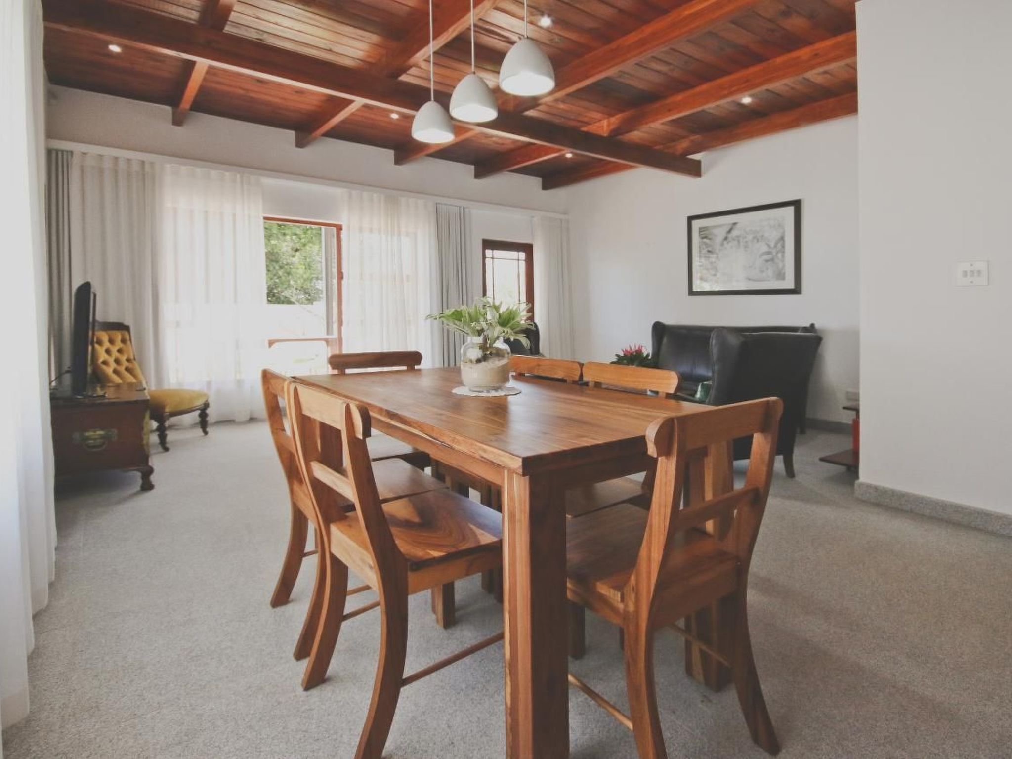 A dining area with a wooden table and chairs, a vase with flowers, and a fireplace in the background.