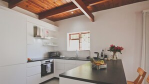 Una cocina moderna con armarios blancos, encimera negra y vigas de madera en el techo. Hay un frutero sobre la encimera y un jarrón con flores.