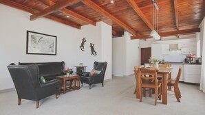 Amplia sala de estar con techo de madera, un sofá de cuero negro, una mesa de comedor de madera con sillas y una cocina al fondo.