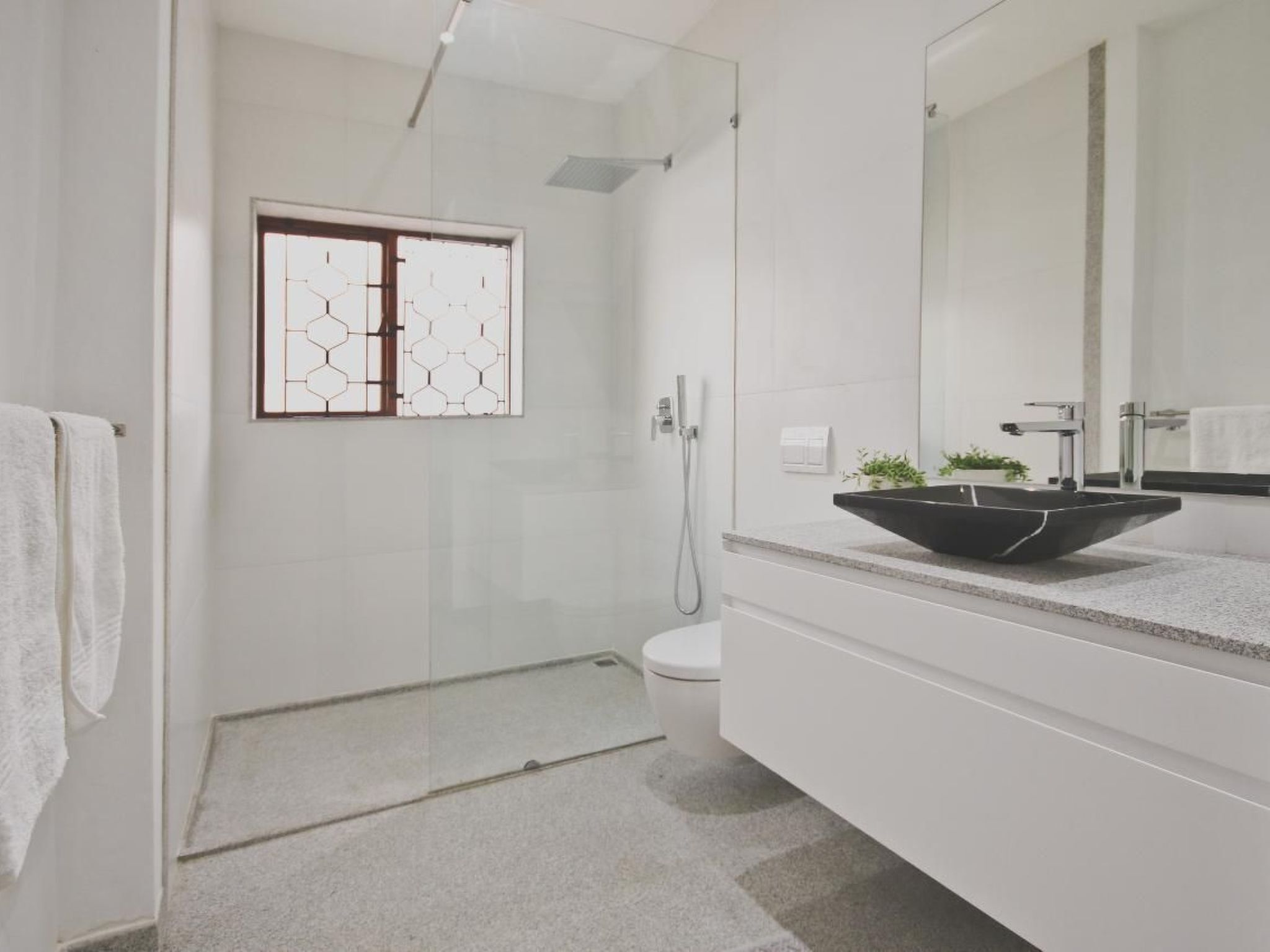 A modern bathroom with a glass shower enclosure, a white toilet, and a large mirror above the sink.