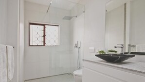 Un baño moderno con cabina de ducha de vidrio, inodoro blanco y un espejo grande sobre el lavamanos.