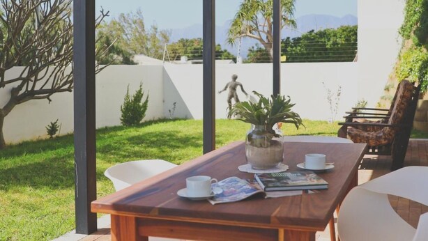 Una mesa de madera con un florero de plantas, sillas blancas y una revista encima.