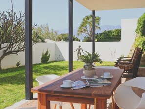 A wooden table with a vase of plants, white chairs, and a magazine on it. - Red Rock Ocean View Villa - Captain's Apartment by Interhome (Gordon's Bay)