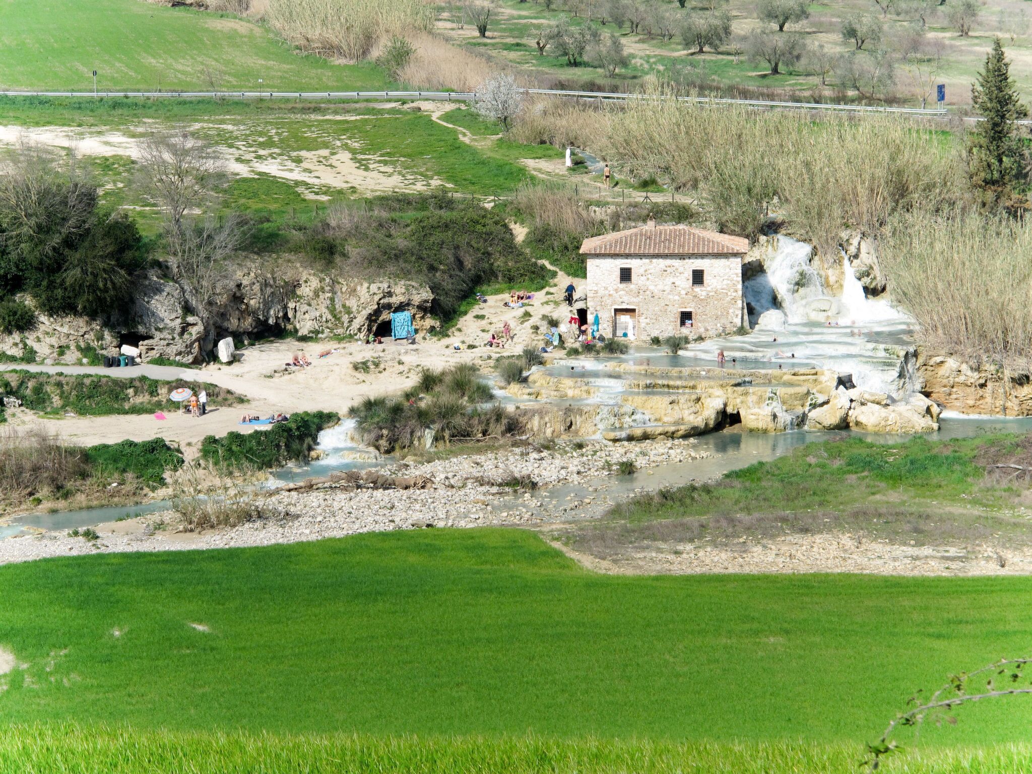 Ein rustikales Steinhaus mit Ziegeldach, gelegen neben einer natürlichen Thermalquellenlandschaft mit Terrassenpools und einem plätschernden Bach.