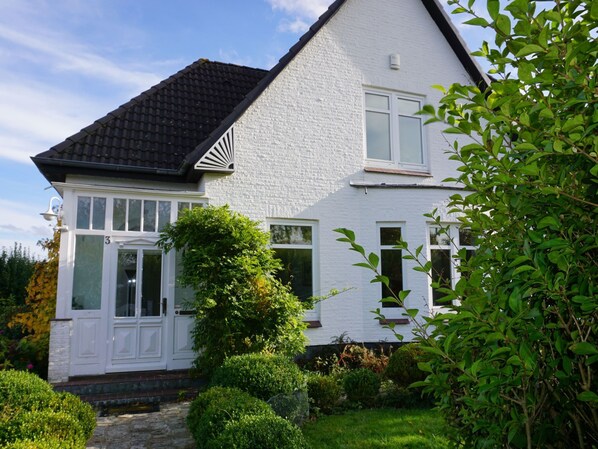 A white two-story house with a black roof, a front door, and a small garden with a pathway leading to the entrance. - Das Meerchenhaus by Interhome (Gelting)