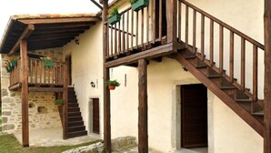 Ein rustikales Steinhaus mit einer Holztreppe und einem Balkon, Steinstufen und einer kleinen Außen-Sitzgelegenheit.