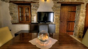 Ein Zimmer mit Steinwänden, einem Holztisch, einem Fernseher und einer Glasglocke als Mittelpunkt.