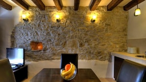 A stone wall with built-in lighting, a dining table with chairs, a fruit bowl, and a television on a stand. - Istrien Traditionelles Steinhaus 6 by Interhome (Buzet)