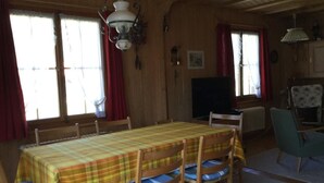 Un comedor con una mesa cubierta por un mantel escocés, sillas de madera con cojines azules y una lámpara colgante.